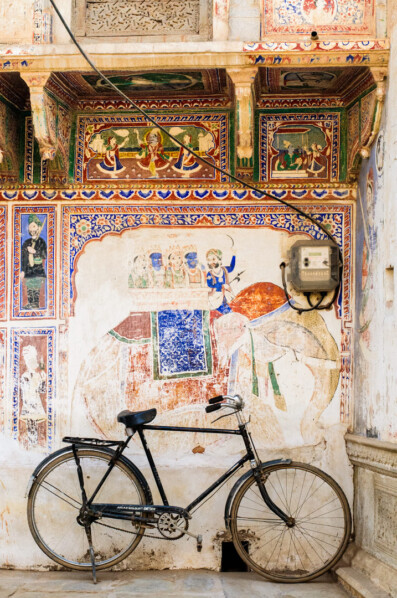 A bicycle is parked against a wall mural in North India