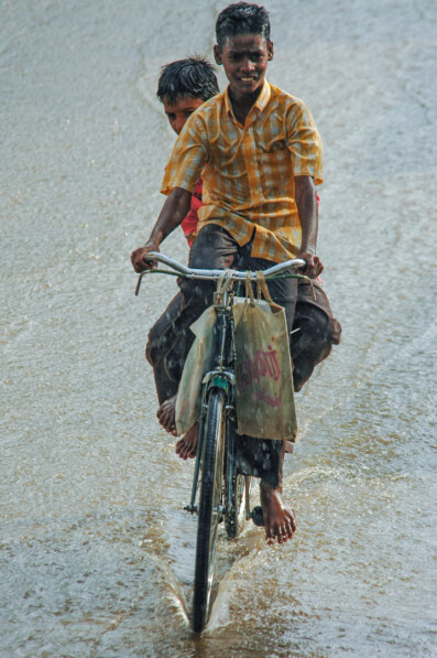 Indian boys enjoy riding a bike through a flooded street
