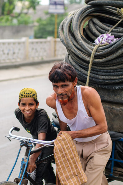 A father and son push a rickshaw loaded with bicycle tires.