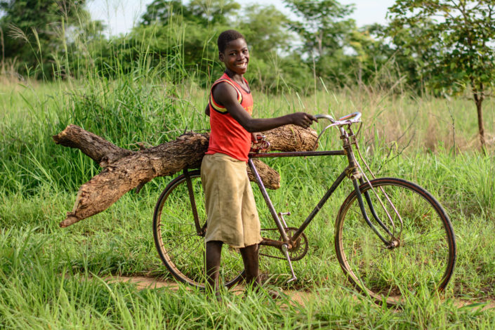 An African boy carries firewood on the back of his bicycle rack.