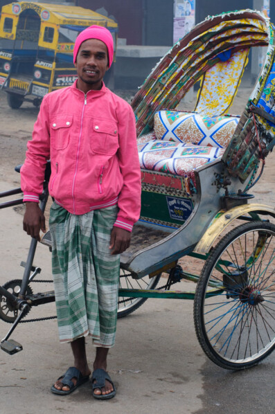 A Bangladeshi chauffeur stands proudly next to his rickshaw