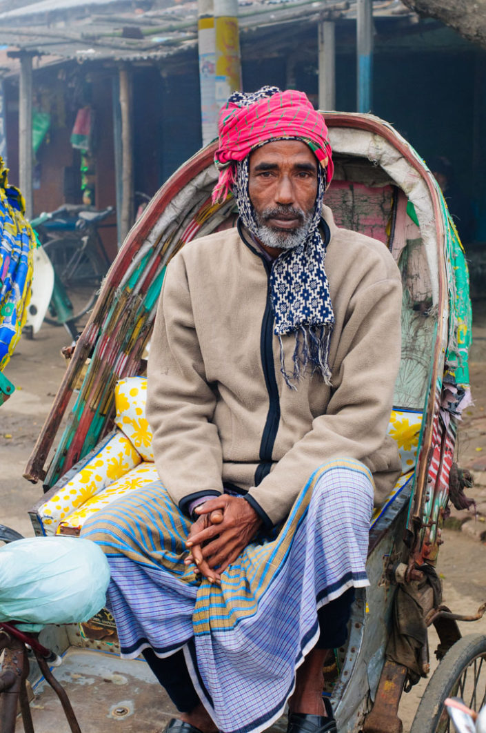 A Bangladesh chauffeur is bundled up for the winter cold while sitting in his rickshaw.