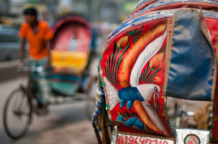 A rickshaw passes another colorful rickshaw in Dhaka