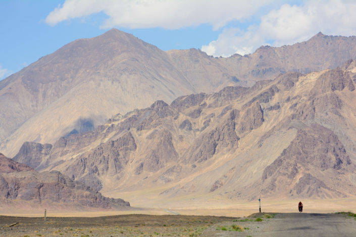 In the distance a small bike rides towards Murgab, Tajikistan.