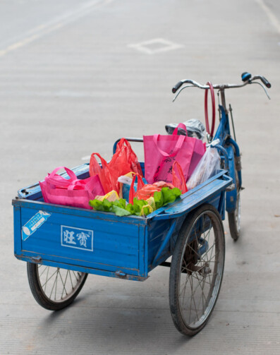 A blue Chinese cargo bike is full of brightly colored bags.