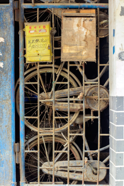 Old dusty bicycles stand behind a gate door in China
