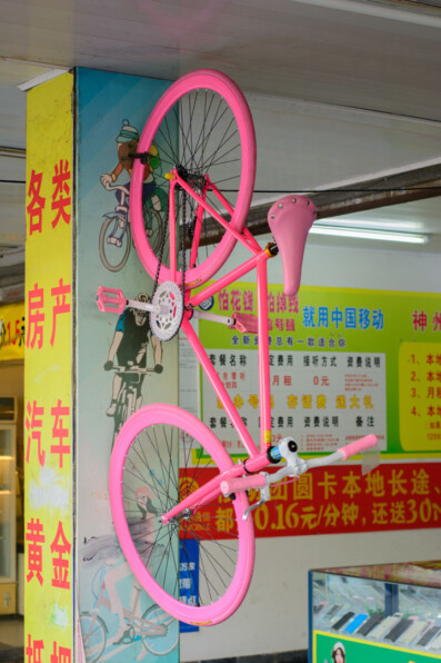 A pink single speed bicycle hangs on a wall in a Chinese shop