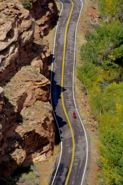 A small red cyclist rides past a rock wall in Utah.