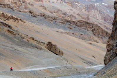 A small red bicyclist pushes their bike up a mountain pass on the Leh Manali highway.