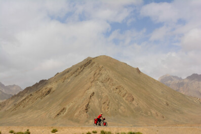A littlle red cyclist pedals past a mountain on the Pamir highway in Tajikistan.