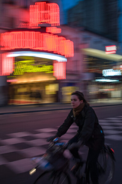 A Paris cyclist rides past a neon sign in the evening hours
