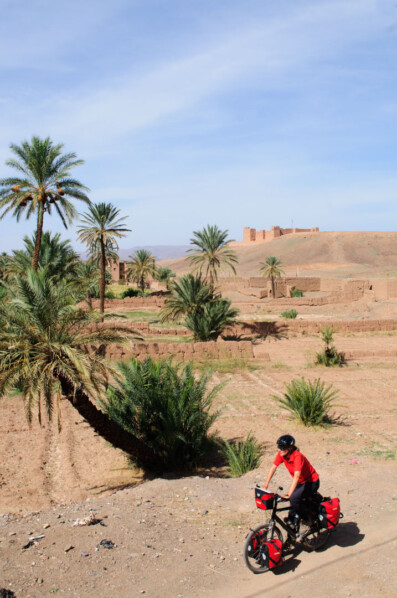 A cyclist rides past palm trees and a casbah in Morocco