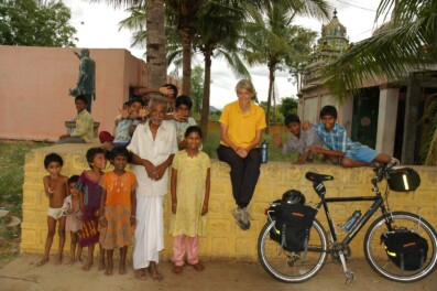 A western cyclist sits on a wall in South India and locals stand next to her.