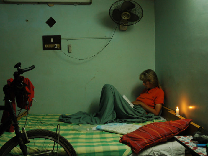 A Western cyclist sits on a hotel bed with a lighted candle in India.