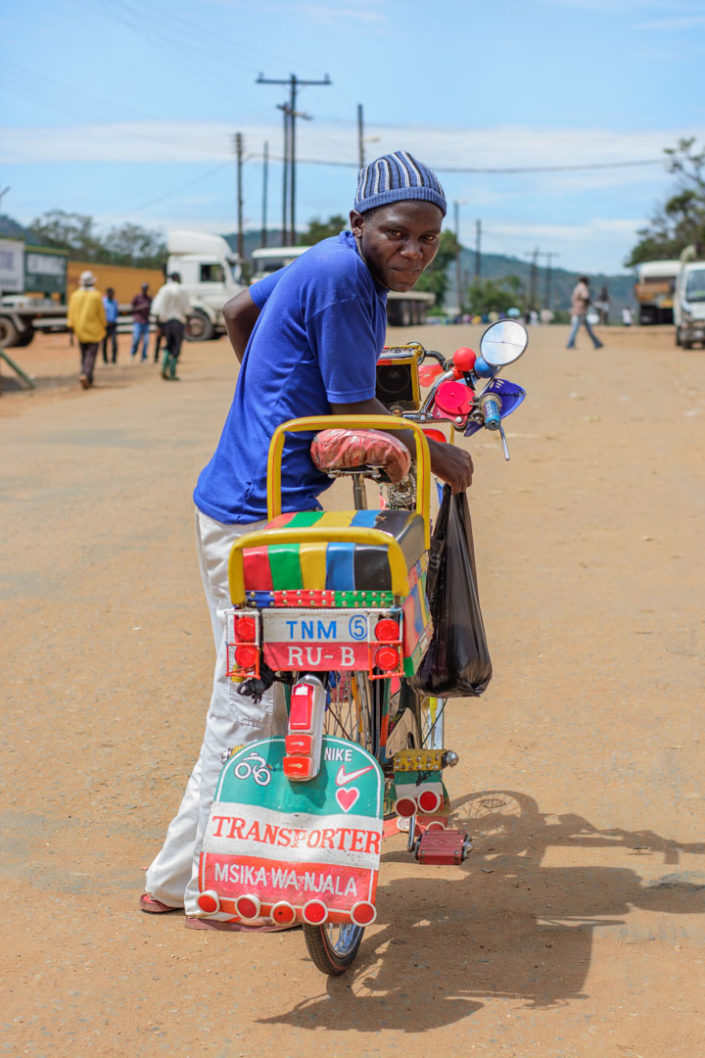 An African bike taxi chauffeur straddles his decorated bicycle.
