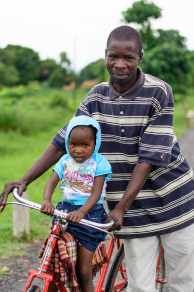 A Malawi father holds his bicycle while his daughter sits on the front tube.