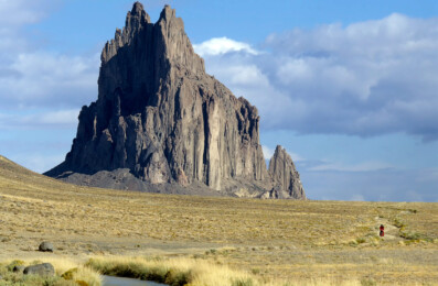 A little red cyclist rides away from Shiprock