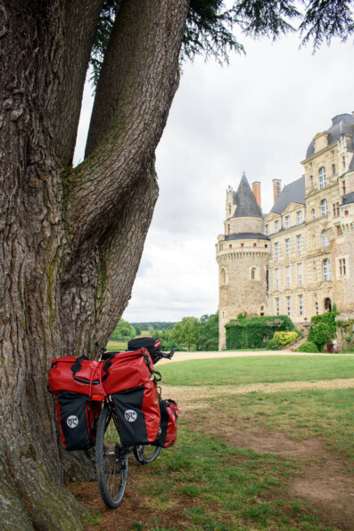 A touring bike leans against a tree with a view over a French castle.