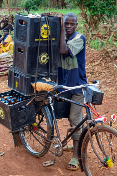 An African stands next to his bicycle that is piled high with crates of beer - bicycle culture