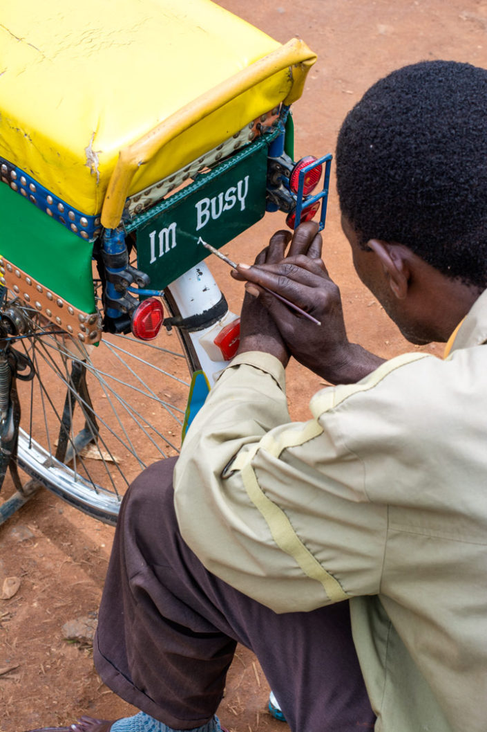 An African man paints text on a bicycle license plate