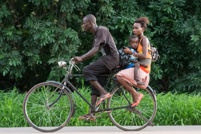 An African bicycle taxi with a mother and her child on the back rack pedal to their destination