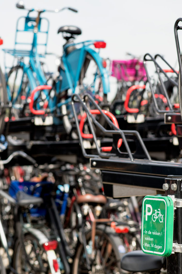 A green dutch bicycle parking sign stands in front of bicycle racks in Amsterdam
