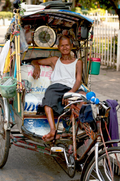 An elderly Rickshaw chauffeur in Thailand waits for a customer