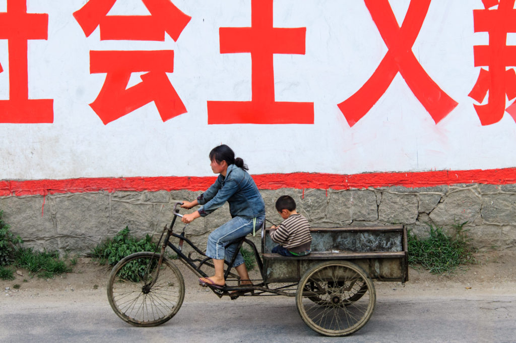 Bicycle culture - A mother and child pedal their cargo bike past a Chinese sign.