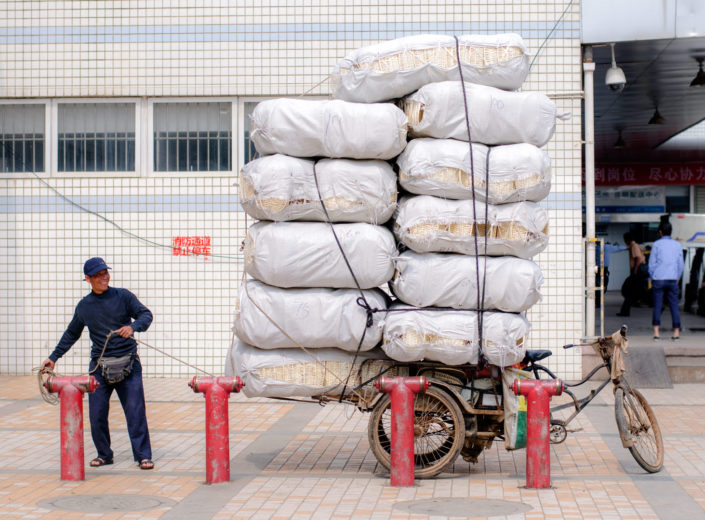 A Chinese man ties huge bags on top of his already overloaded bike rickshaw.