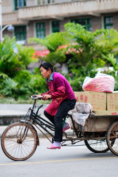 A Chinese woman furiously pedals her cargo bike.